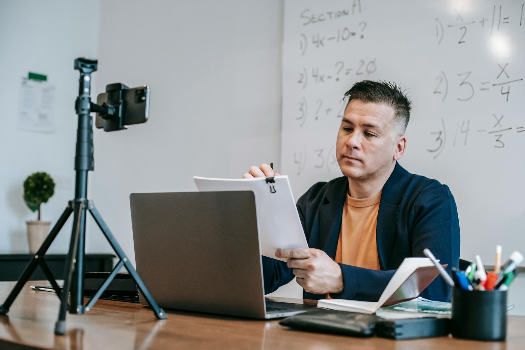 Professional educator engaging in online teaching session with laptop and camera setup indoors.